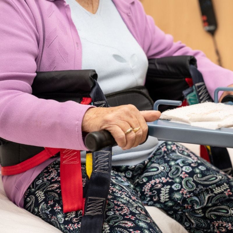 Woman grasps handles with sling around torso.