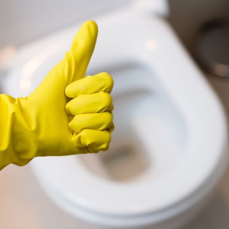 Yellow gloved hand gives thumbs up over toilet bowl.