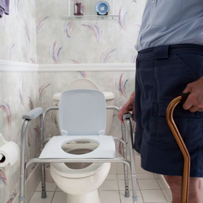 Person with cane holds onto toilet seat riser in bathroom.