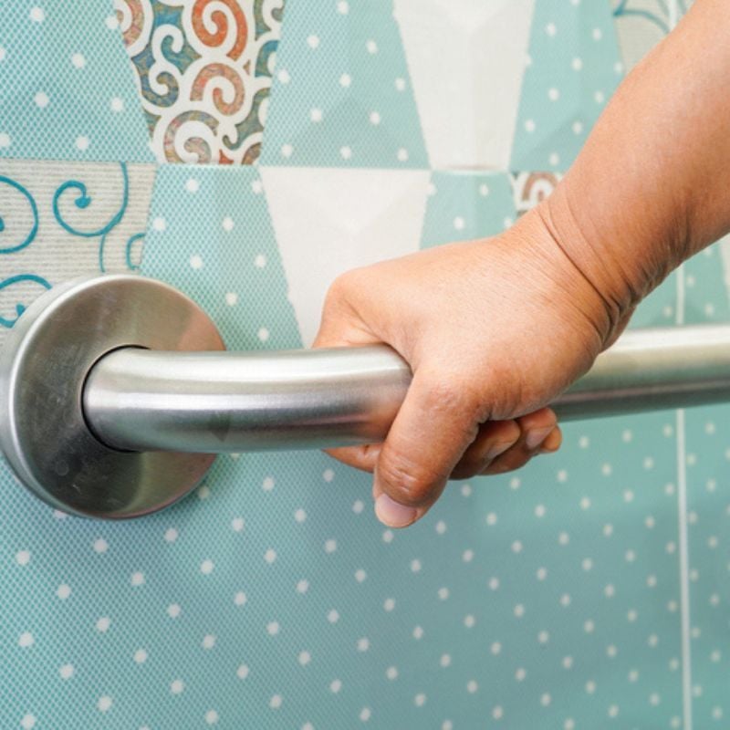 Hand grabs metal grab bar in bathroom.