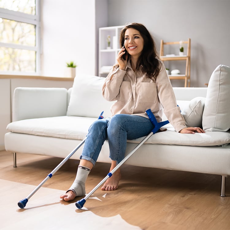 Woman with ankle splint and crutches calls APA Medical from home for equipment support