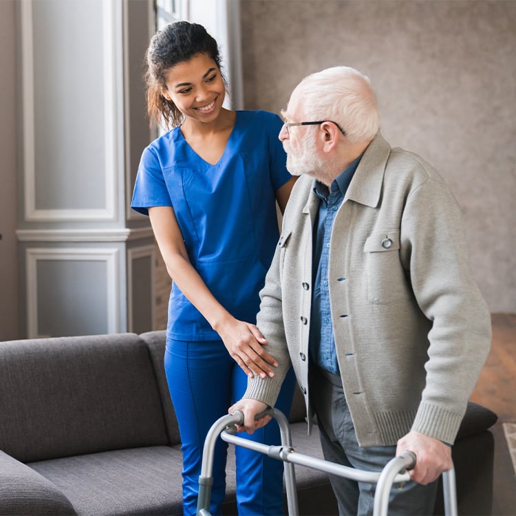 Caregiver smiling as she walks beside older male patient using a walker for support