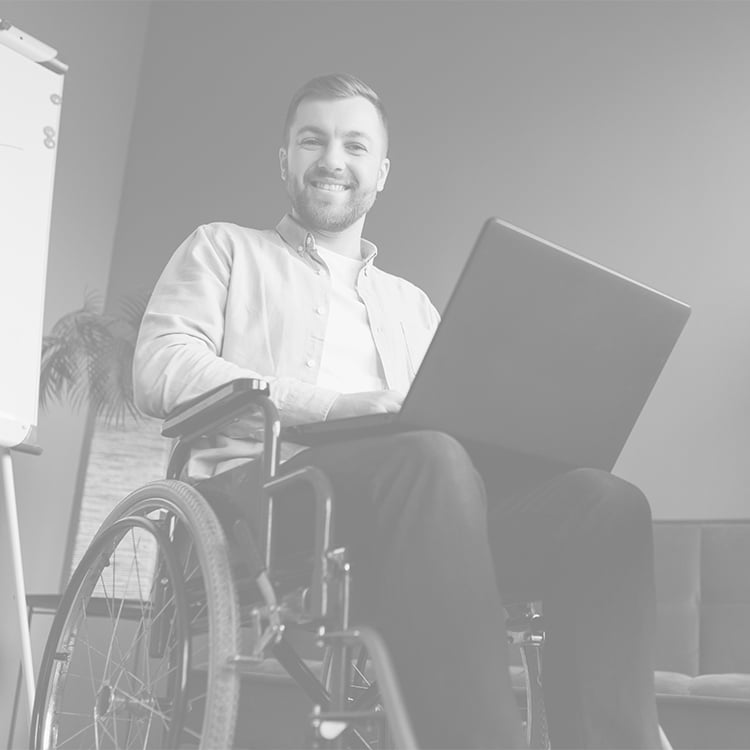 Man in wheelchair smiles at camera while typing on laptop resting on his lap